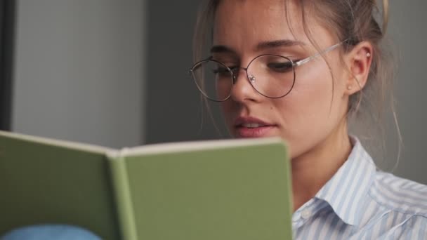 一个戴着眼镜 正在做梦的年轻女子的近照是 她正坐在家里的沙发上 在笔记本上记笔记 — 图库视频影像