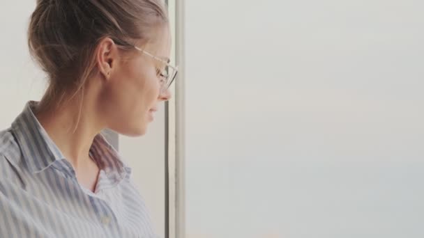 Μια Ήρεμη Γυναίκα Γυαλιά Κοιτάζει Έξω Από Παράθυρο Του Σαλονιού — Αρχείο Βίντεο