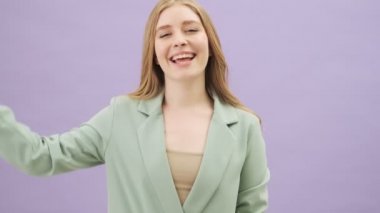 Dost canlısı genç bir kadın, gri arka planda tek başına dikilirken baş parmak hareketi yapıyor.