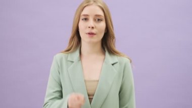 Gri arka planda tek başına duran hoş, genç bir bayan sessizlik jesti yapıyor.