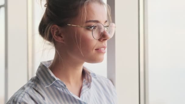 Widok Bliska Spokojnej Młodej Kobiety Okularach Wygląda Przez Okno Stojącej — Wideo stockowe