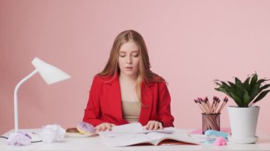 Hoşnutsuz genç bir kadının iş yerinde pembe arka planda soyutlanmış bir masada otururken sorunları var.