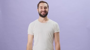 Beyaz tişört giyen çekici bir genç, gri arka planda tek başına dikilirken başparmağını kaldırıyor.
