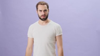 Beyaz t-shirt giyen kızgın genç bir adam, gri arka planda tek başına dikilirken birine bağırıyor.