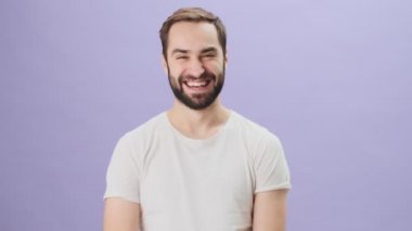 Beyaz tişört giyen mutlu, genç bir adam gri arka planda tek başına dikilip gülüyor.