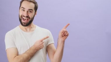 Beyaz tişört giyen mutlu bir genç adam, iki eli de gri arka planda tek başına duran boş alanı gösteriyor.