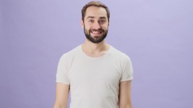 Beyaz tişörtlü mutlu bir genç adam gri arka planda tek başına dikiliyor.