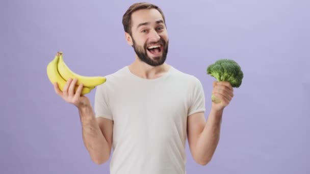 Attraktiv Ung Man Bär Vit Shirt Håller Banan Och Broccoli — Stockvideo