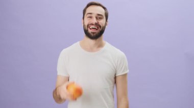 Beyaz tişört giyen mutlu genç bir adam, gri arka planda tek başına duran portakal rengi bir jest yapıyor.