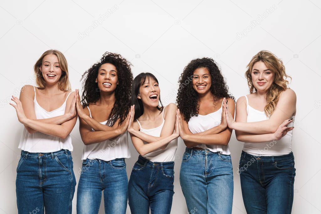 Image of joyful multinational women in blue jeans smiling and holding hands together isolated over white background