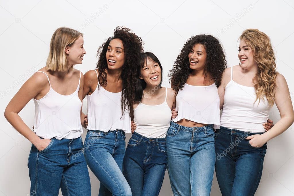 Image of joyful multinational women in blue jeans smiling and hugging together isolated over white background