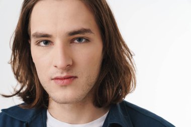 Beyaz arka planda izole edilmiş, uzun saçlı, poz veren ve kameraya bakan çekici bir genç resmi.