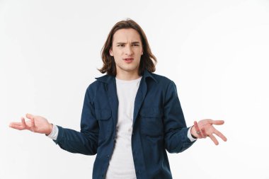 Kafası karışmış, uzun saçlı, poz veren ve beyaz arka planda el kaldıran genç bir adam resmi.