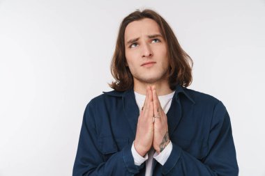 Kafkasyalı üzgün, uzun saçlı, yukarı bakan ve avuç içlerini beyaz arka planda bir arada tutan bir adam.