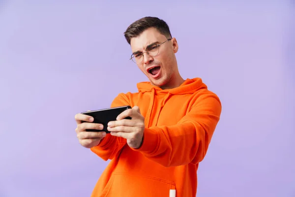 感情的な集中叫んで若い男の肖像画は 携帯電話で紫色の背景ゲームを上に孤立ポーズ — ストック写真