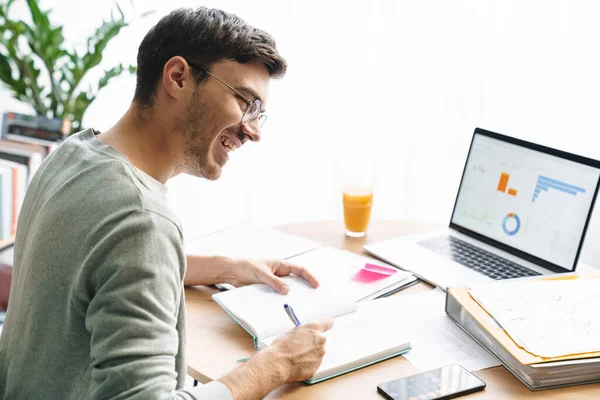 Obraz Szczęśliwy Młody Człowiek Okularach Robi Obliczenia Podczas Pracy Laptopie — Zdjęcie stockowe