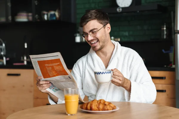 Sabahları Mutfakta Oturup Gazete Okurken Bornoz Giymiş Gülümseyen Genç Adam — Stok fotoğraf