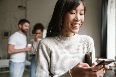 Ofiste birlikte çalışan çok ırklı genç iş adamlarının görüntüsü. Cep telefonu kullanan kadın