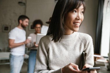 Ofiste birlikte çalışan çok ırklı genç iş adamlarının görüntüsü. Cep telefonu kullanan kadın