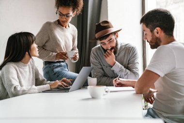 Çok ırklı genç bayan ve erkek meslektaşların ofiste çalışırken masada iş fikirlerini tartışmaları