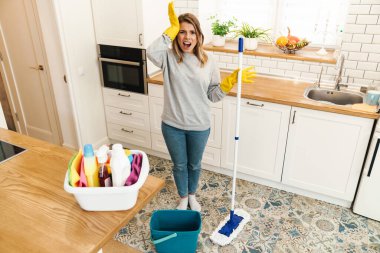 Photo of irritated woman housewife in gloves screaming while mopping floor at modern kitchen clipart