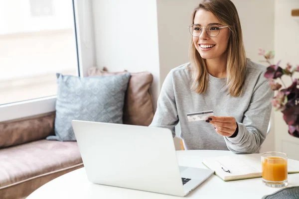 Foto Mulher Sorridente Óculos Usando Laptop Enquanto Segurando Cartão Crédito — Fotografia de Stock