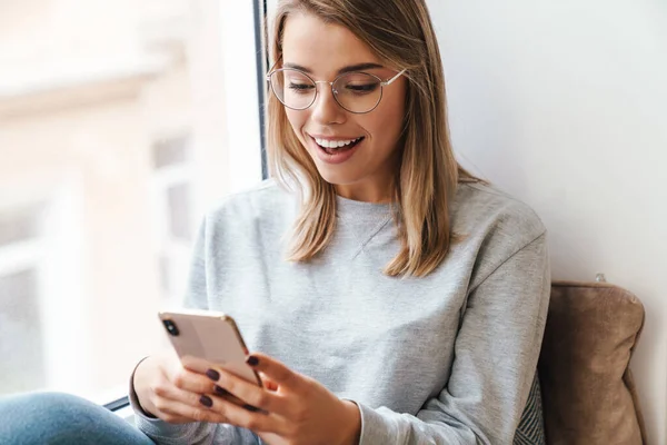 Pencere Kenarında Otururken Akıllı Telefon Kullanan Gözlüklü Güzel Bir Kadının — Stok fotoğraf