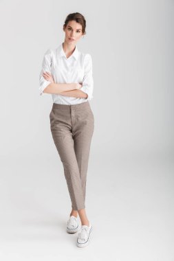 Beyaz arka planda, elleri çaprazlanmış bir şekilde poz veren genç bir kadın resmi.