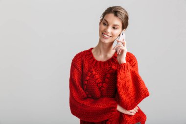 Kırmızı kazaklı, gülümseyen ve beyaz arka planda cep telefonuyla konuşan neşeli bir kadın resmi.