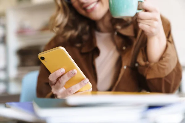 Imagem Sorrindo Mulher Agradável Óculos Chapéu Usando Celular Enquanto Bebe — Fotografia de Stock