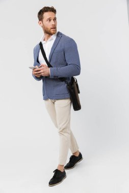 Beyaz arka planda tek başına yürürken cep telefonu kullanan ceketli ciddi bir genç resmi