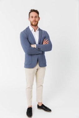 Ceket giyen, elleri çaprazlanmış bir şekilde kameraya poz veren mutlu genç bir adamın görüntüsü beyaz arka planda izole edilmiş.