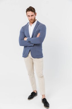 Tıraşsız, ceketli ve elleri çapraz pozlu genç bir adam resmi beyaz arka planda izole edilmiş.