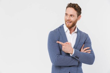 Ceket giyen, gülümseyen ve parmak gösteren neşeli genç adam görüntüsü beyaz arka planda izole edilmiş.