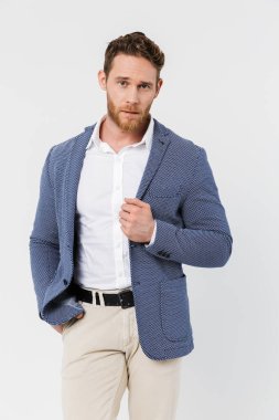 Ceket giyen sakallı genç bir adam resmi. Beyaz arka planda izole edilmiş kameraya bakıyor ve poz veriyor.