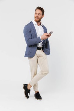 Beyaz arka planda izole edilmiş, gülümseyen ve akıllı telefon kullanan ceketli, neşeli yakışıklı bir adam görüntüsü.