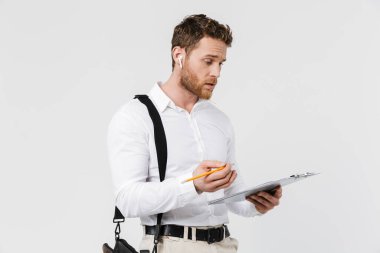 Kablosuz kulaklıklı, elinde not panosu olan ve beyaz arkaplanda izole edilmiş yazı yazan kafası karışmış bir adam resmi