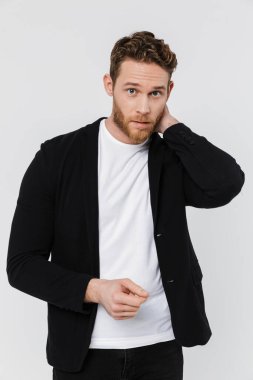 Tıraşsız, kafası karışmış, beyaz arka planda poz veren ve kameraya bakan bir adam resmi.