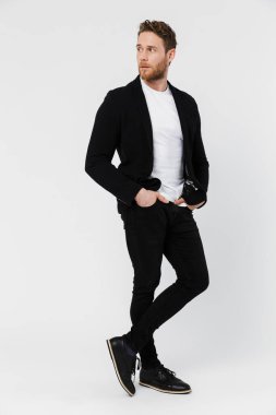 Tıraşsız, ceketli, beyaz arka planda yalnız bir şekilde poz veren ve bakan ciddi bir adamın görüntüsü.