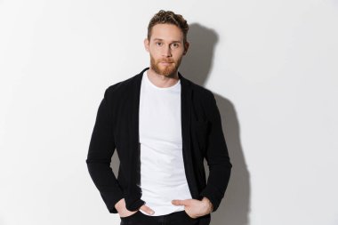 Beyaz arka planda izole edilmiş, ceketli, poz veren ve kameraya bakan traşsız, kendine güvenen bir adam görüntüsü.