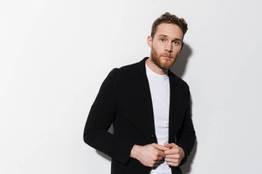 Beyaz arka planda izole edilmiş, ceketli, poz veren ve kameraya bakan traşsız, kendine güvenen bir adam görüntüsü.