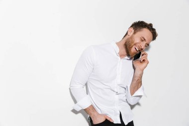 Tişörtlü, mutlu, yakışıklı bir adamın görüntüsü cep telefonuyla konuşuyor ve beyaz arka planda izole bir şekilde gülüyor.