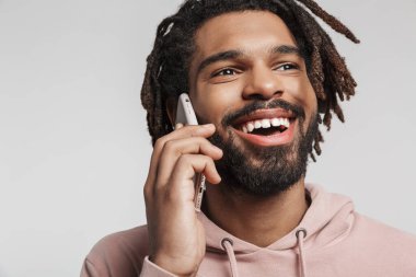Beyaz arka planda izole edilmiş, cep telefonuyla konuşan, kapüşonlu, gülümseyen, genç bir Afrikalı adamın portresini kapat.