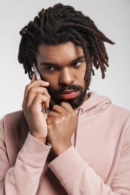 Kapüşonlu genç bir Afrikalı 'nın portresi. Beyaz arka planda tek başına duruyor, cep telefonuyla konuşuyor.