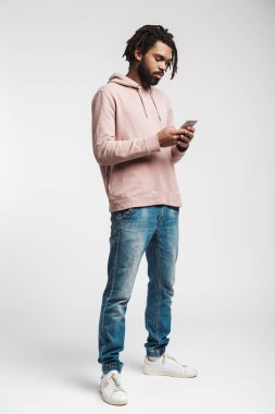 Beyaz arka planda izole edilmiş bir şekilde duran ve cep telefonu kullanan odaklanmış Afrikalı Amerikalı bir adamın portresi.