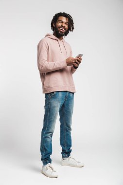 Beyaz arka planda izole edilmiş, gülen ve cep telefonu kullanan neşeli Afrikalı Amerikalı adamın portresi.