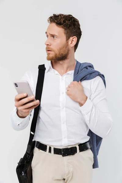在白色背景下 一个全神贯注的金发男人拿着夹克 用手机打字的图片 — 图库照片