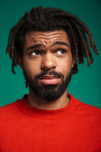 Close up portrait of a young african man wearing pullover standing isolated over green background, looking away