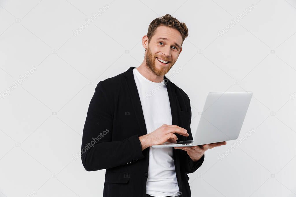 Image of handsome pleased man in jacket smiling and using laptop isolated over white background