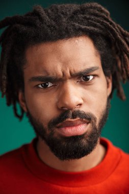 Hoşnutsuz Afro-Amerikan bir adamın portresi. Yeşil arka planda izole edilmiş poz veriyor ve kameraya bakıyor.